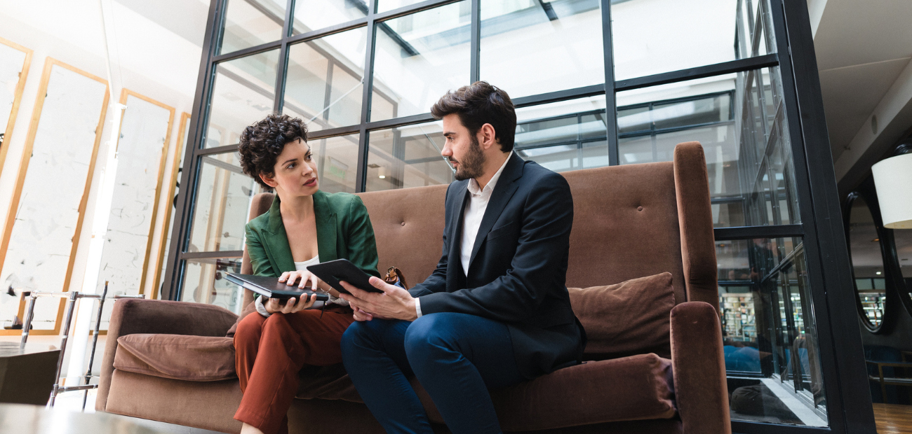 Two business people sitting down on a couch talking to one another