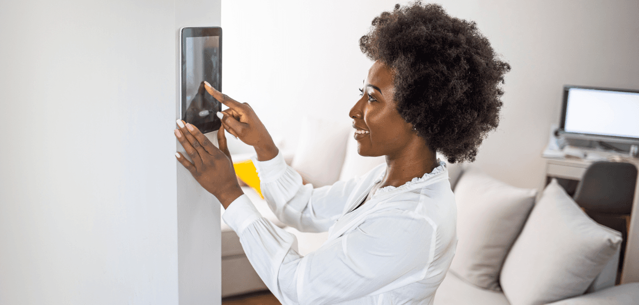 Young african girl woman lady adjusting remote climate control panel settings wall touch screen set heating conditioning switch 