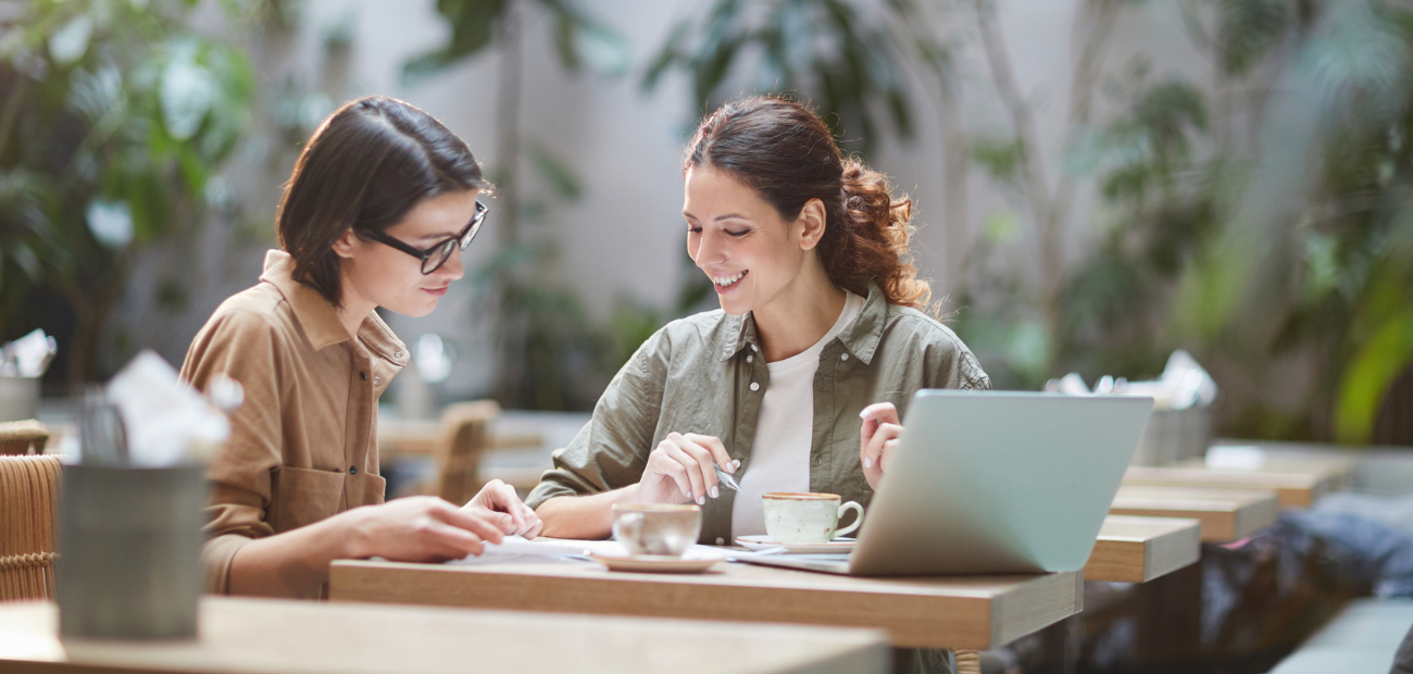 Portrait of two cheerful young omen enjoying work in beautiful outdoor cafe, coffee space