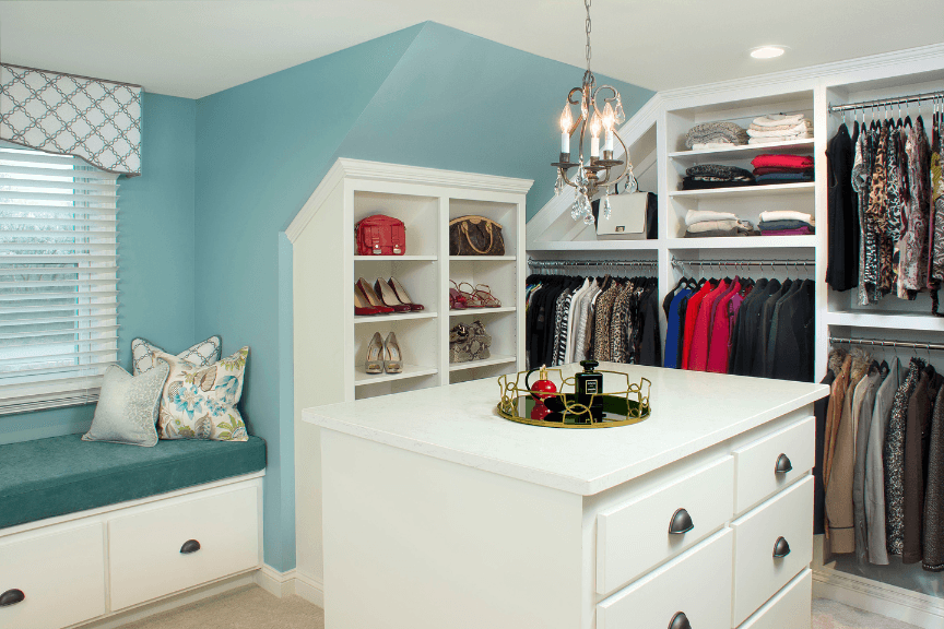 A walk-in closet with dresser, several open shelves and a window seat