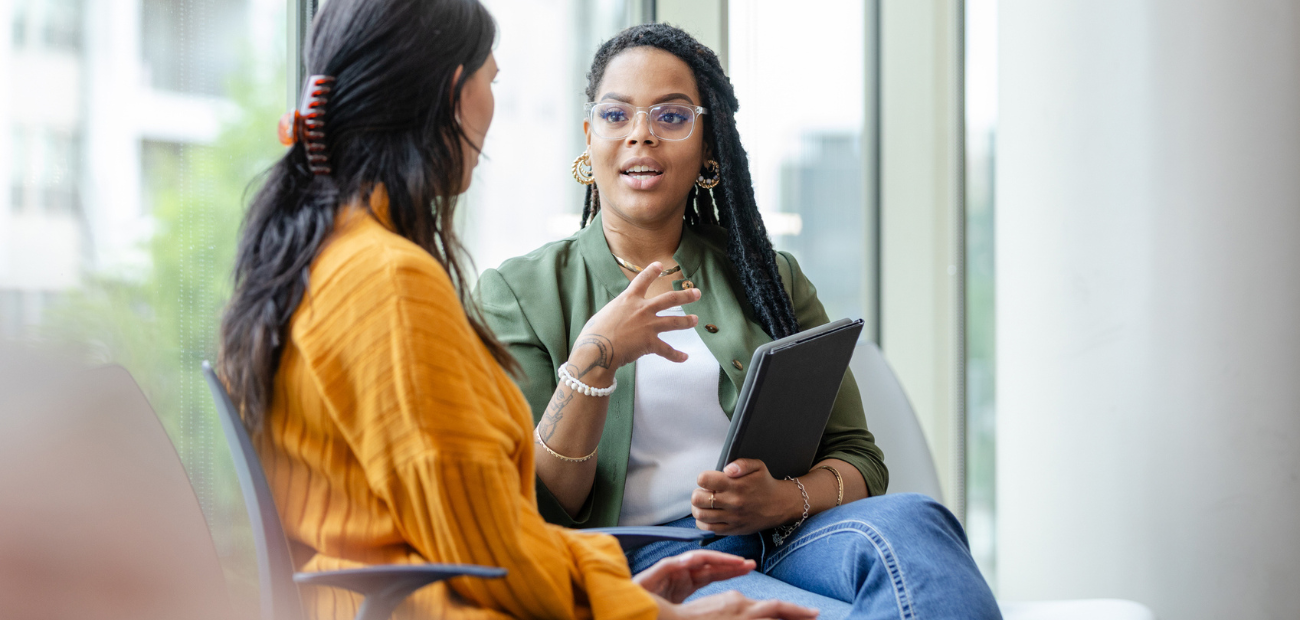 Two businesswomen sitting down, talking to one another about the challenges of their businesses