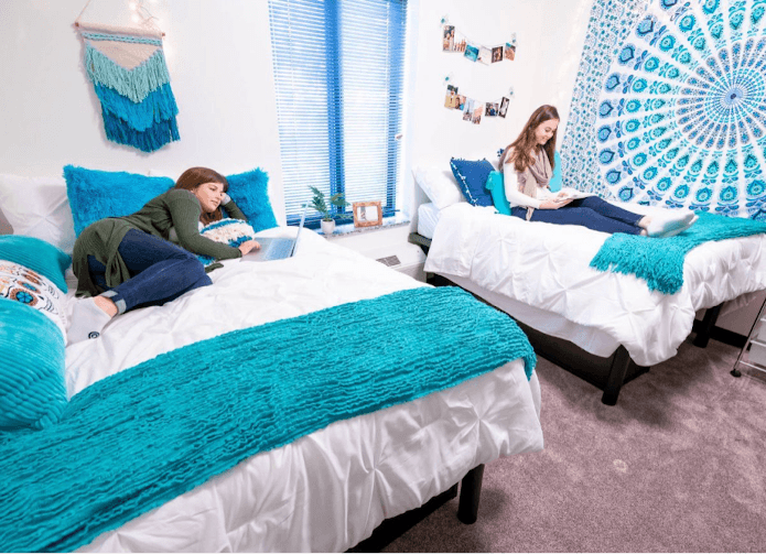 A staged dorm bedroom with tile and white sheets and two people on the beds.