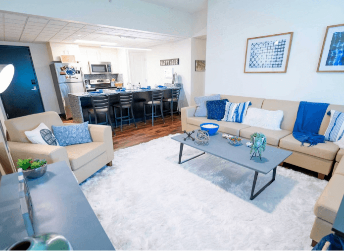 A view of a staged dorm room where you can see a bar kitchen in the background.