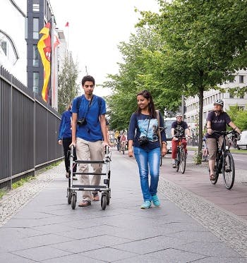 Man walking on a sidewalk in a urban area with the help of a walker