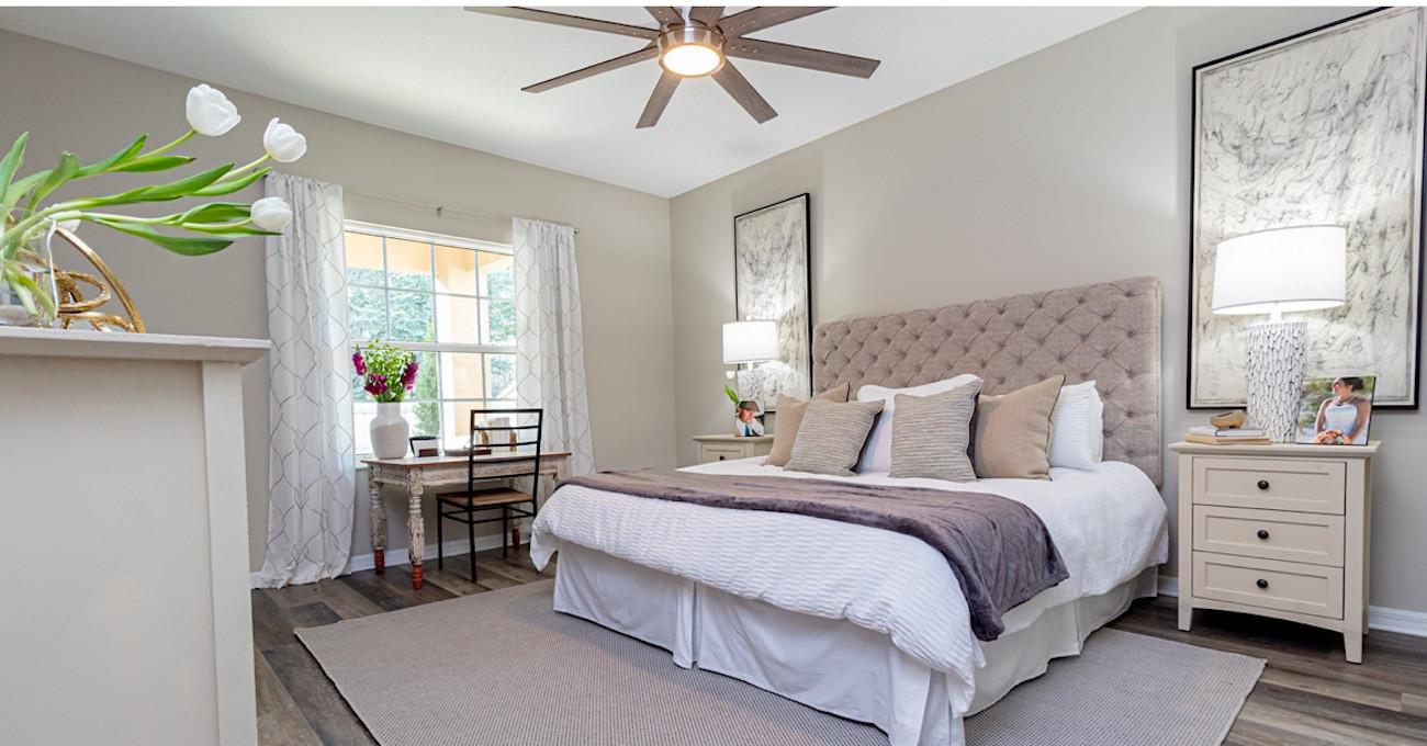 A Bedroom with window, ceiling fan, and sand colored accents.