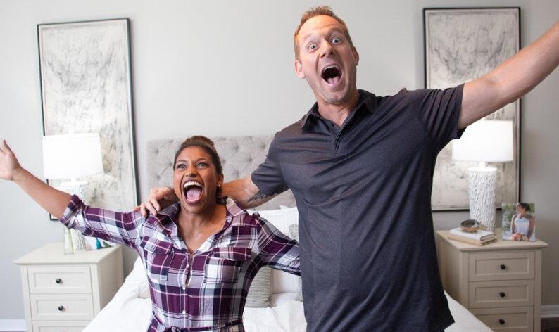 Happy Couple excited in front of a bed, raising their arms and shouting