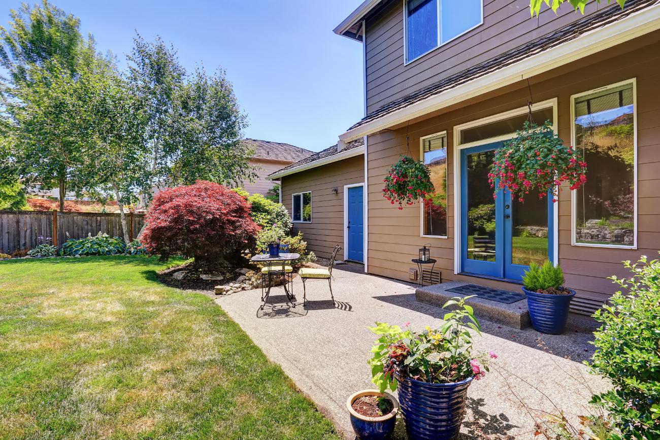 2 story house with backyard patio, blue trim and green lawn.