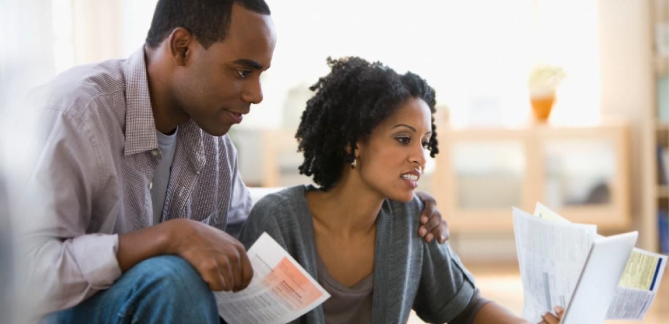 A man and a woman sit in a living room reviewing bills and other documents.