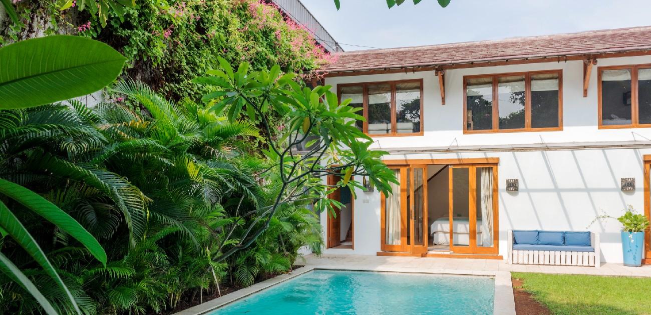 A picture of a home's backyard with a pool, and trees and plants to the left side.