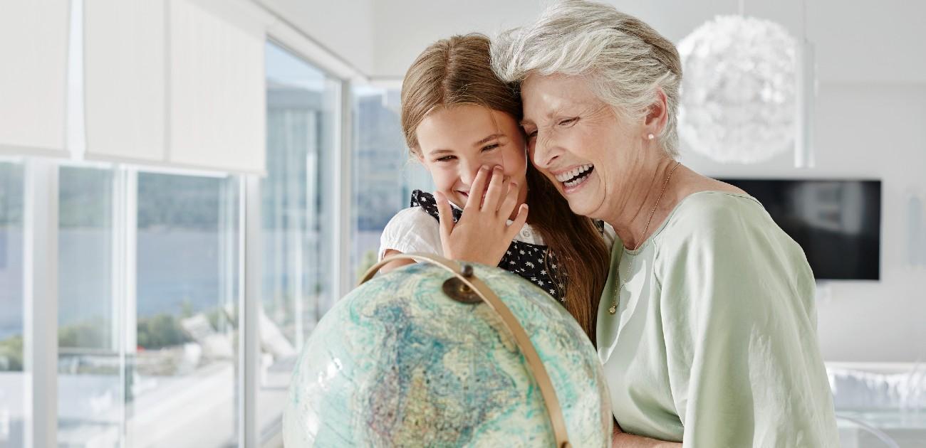 A young girl sitting and laughing with an elderly woman to the right also laughing.