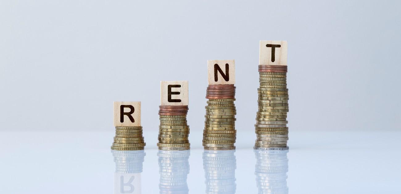 Four stacks of coins from left to right growing taller with wooden letter pieces atop each one, spelling "RENT"