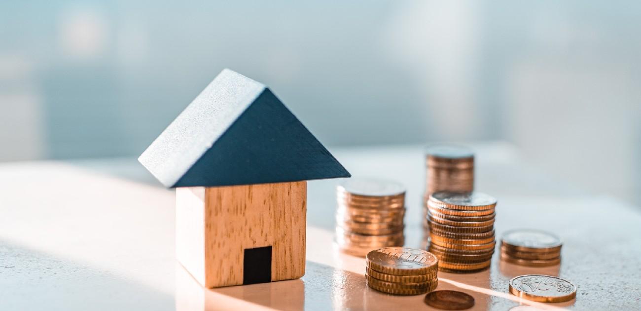 A house miniature next to stacks of coins.