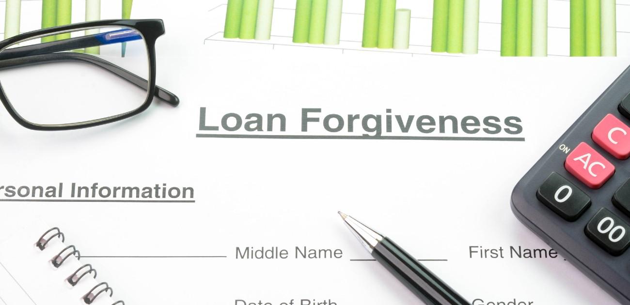 A picture of a loan forgiveness form, with glasses, a pen, and a calculator partially in frame.