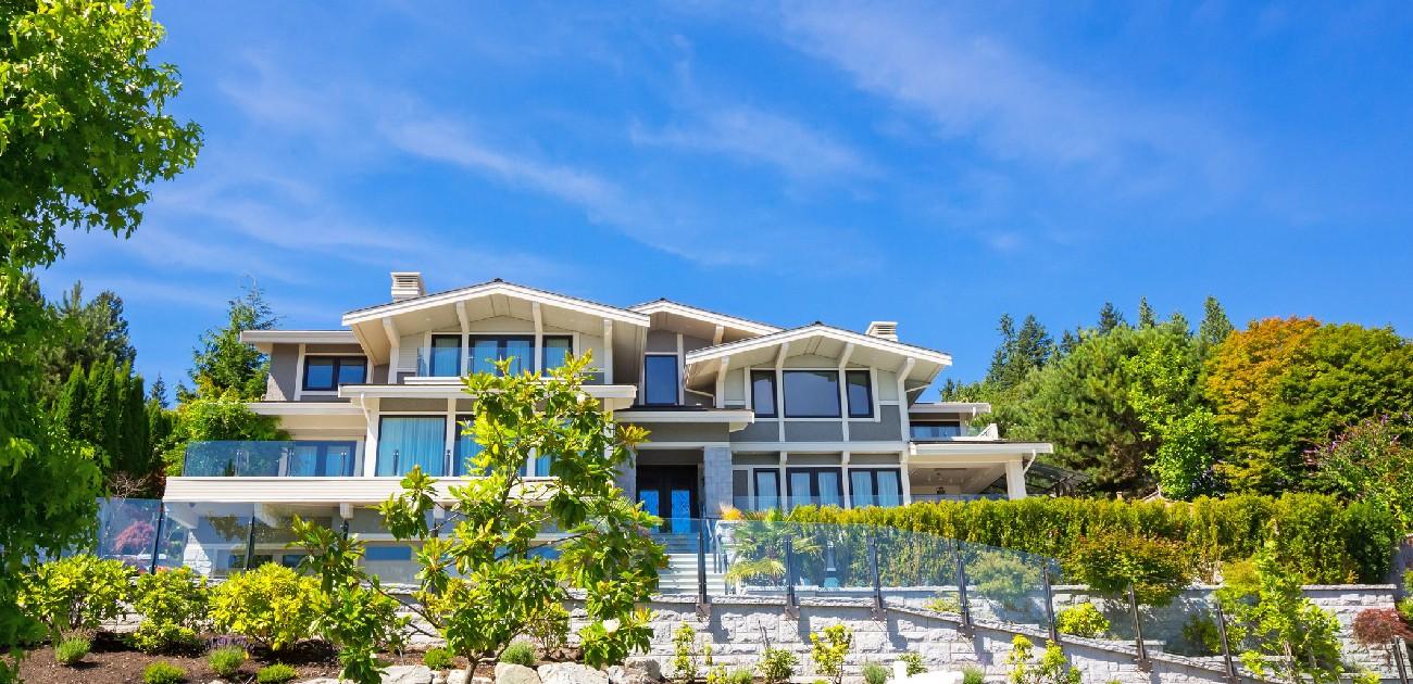 A picture of a luxury home with trees and shrubbery surrounding the wealthy property.