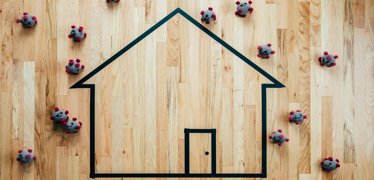 outline of home on wood floor surrounded by "covid" virus cells