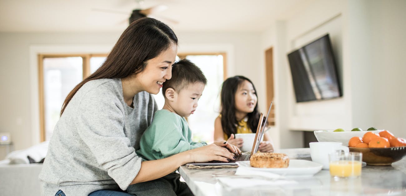 Mother multi-tasking with young children in kitchen table.