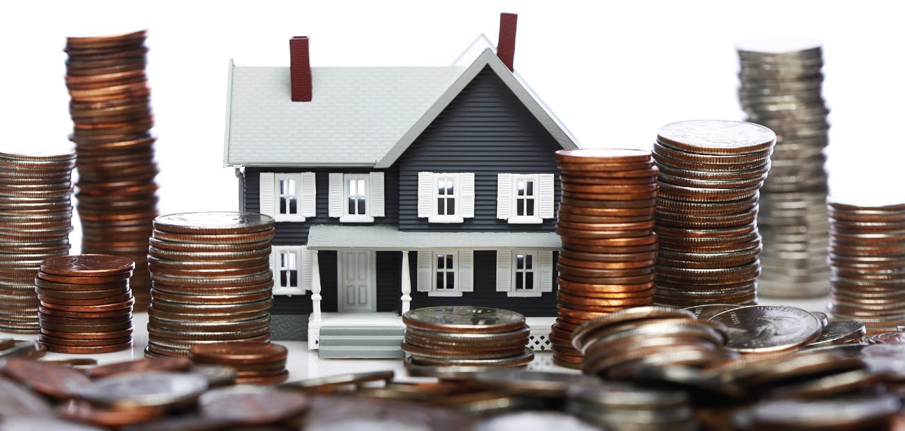 A small model house surrounded by stacks of quarters, pennies, and other coins