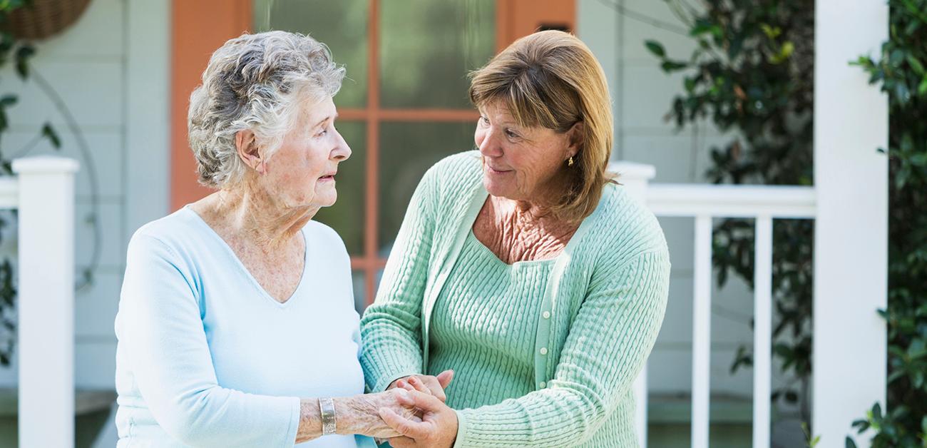 Elderly woman walking with adult daughter in front of house.