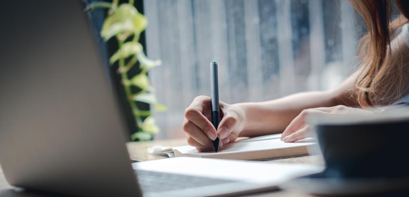 Woman writing a letter in front of a laptop