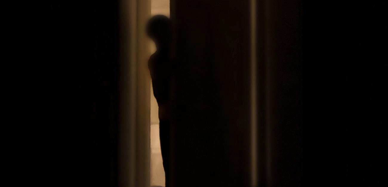 silhouette of person peeking into dark room through a cracked door