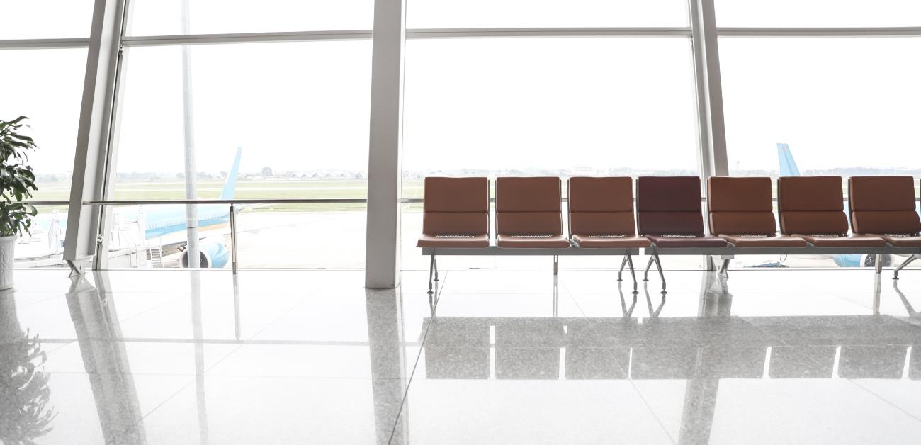 A picture of an airport interior, showing a row of seating along in front of a large window wall out to the tarmac.