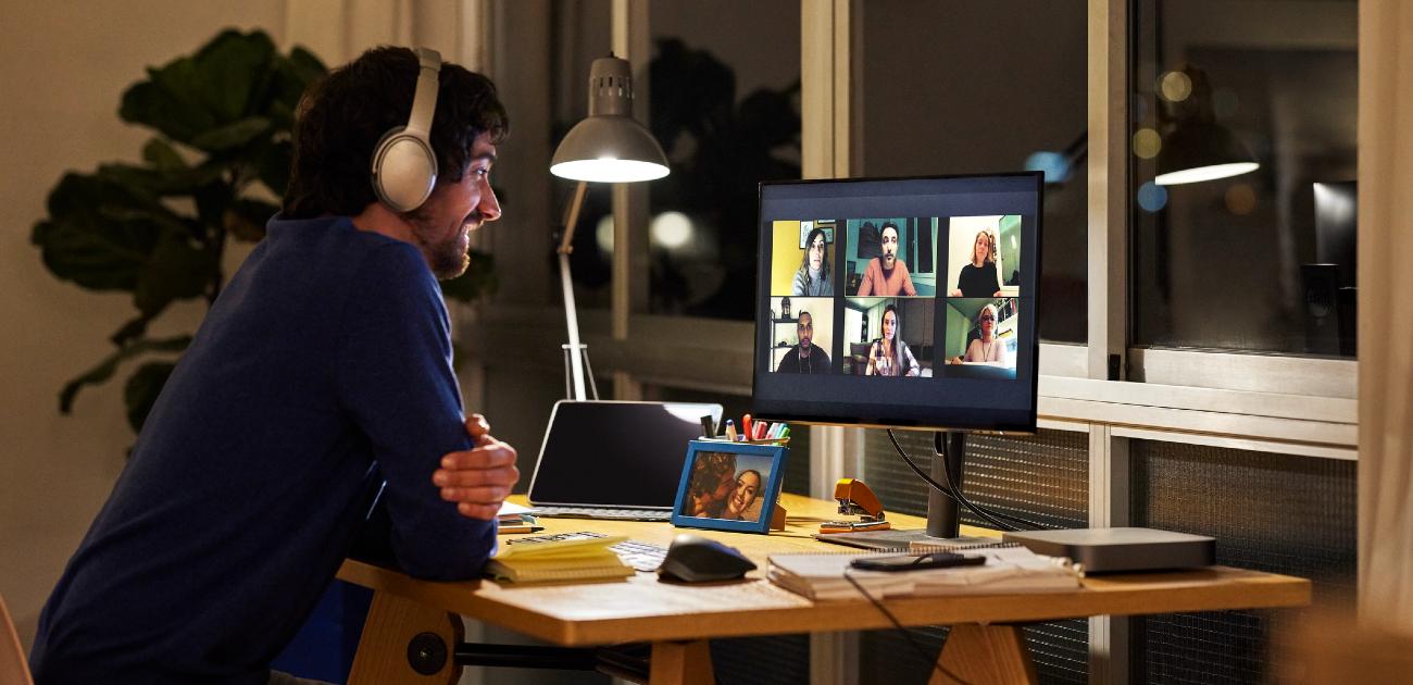 A man toward the left of the image sits at his desktop computer on an evening video call.