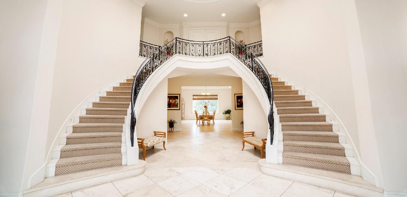 A picture of a mansion's interior with two curved staircases on either side of the entrance.