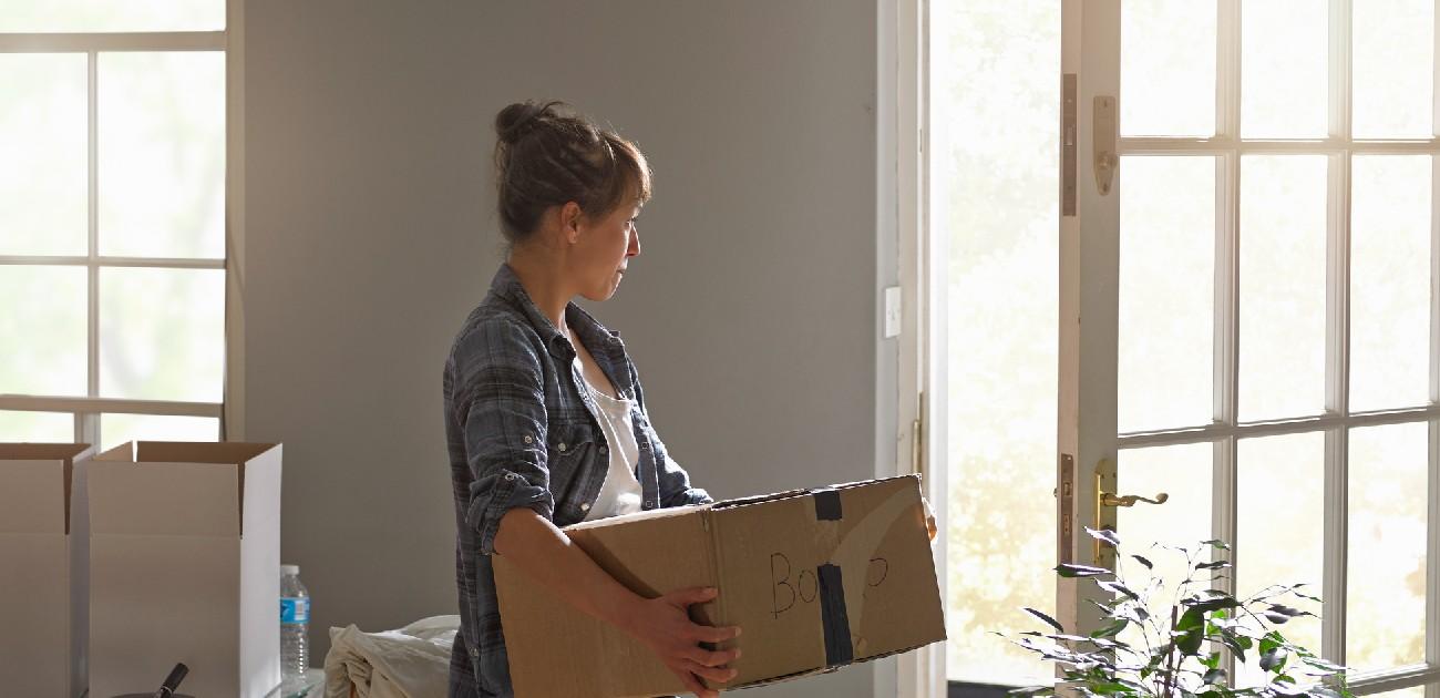 A woman moving into a new home carries a box through a room with various mo