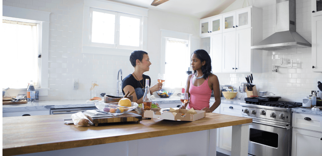 Two friends standing at kitchen island with wine and pizza