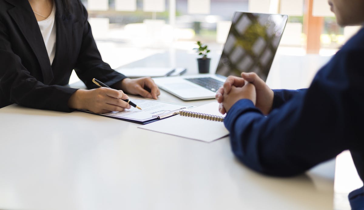 Close Up of Real Estate Agent and Client with Paperwork and Laptop