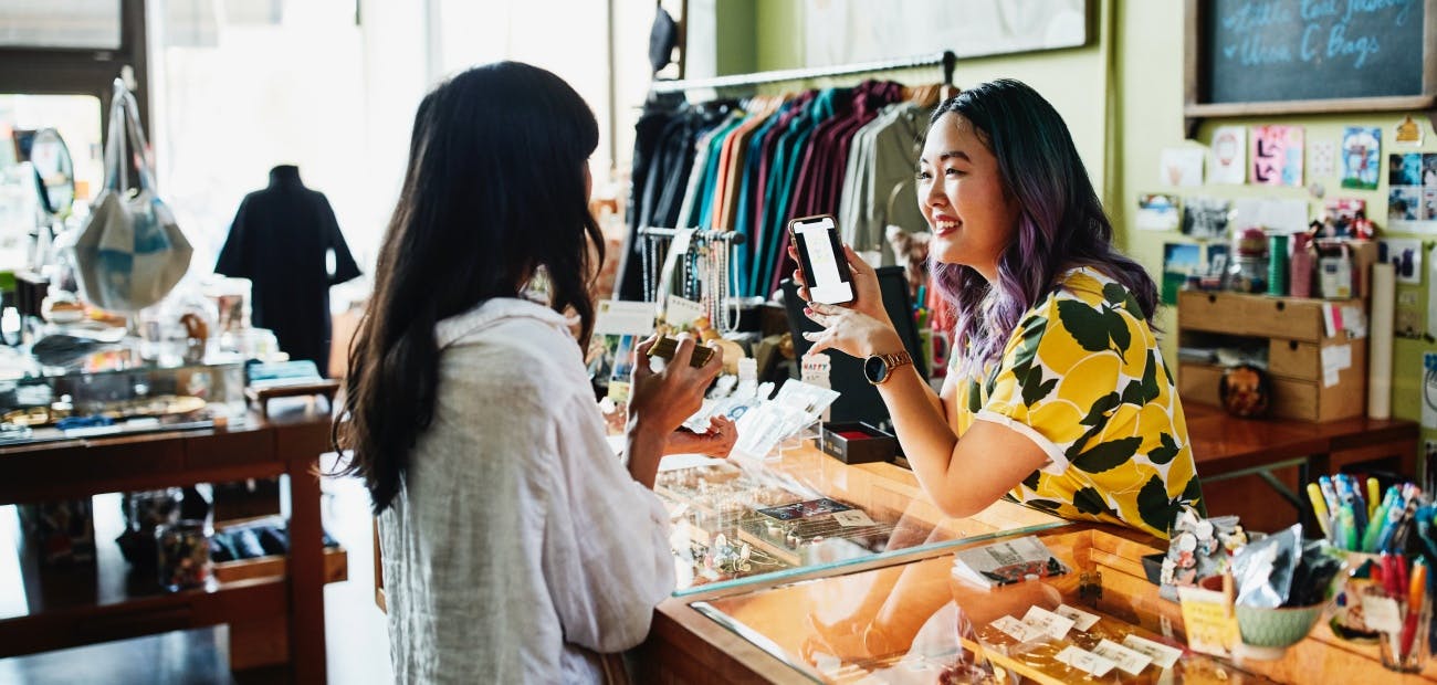 Smiling shopkeeper helping client at counter in boutique