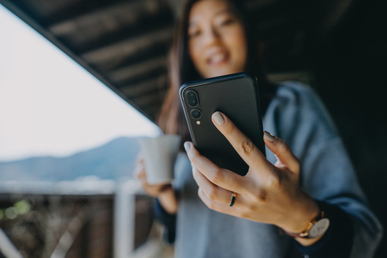 Young woman using smartphone on balcony with coffee