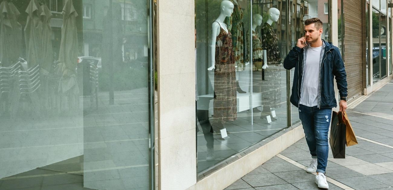 Man walking by storefronts with shopping bags