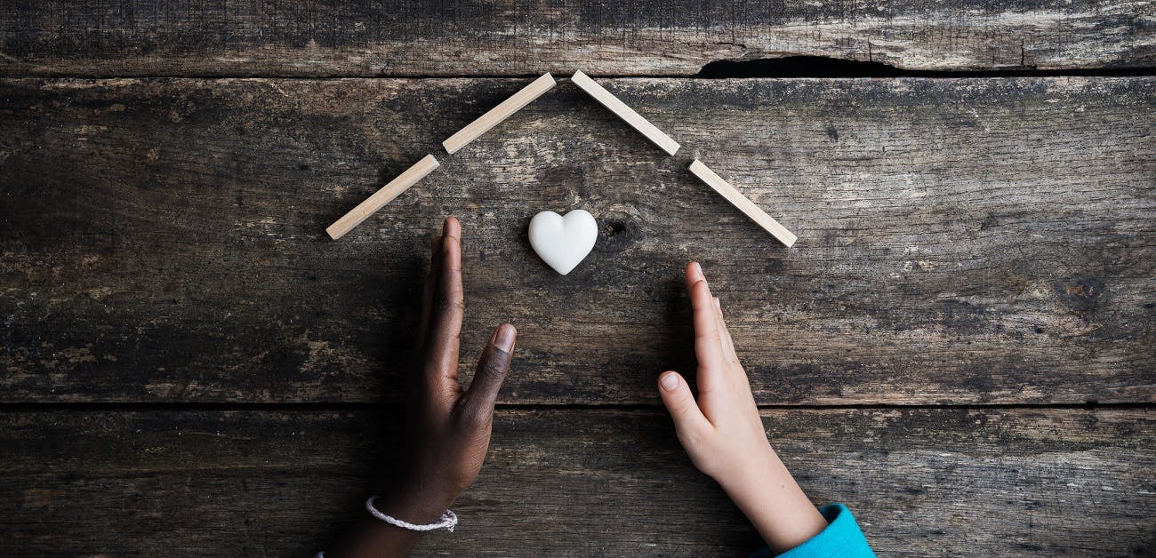 Hand of black and white kids making a house with heart shaped marble