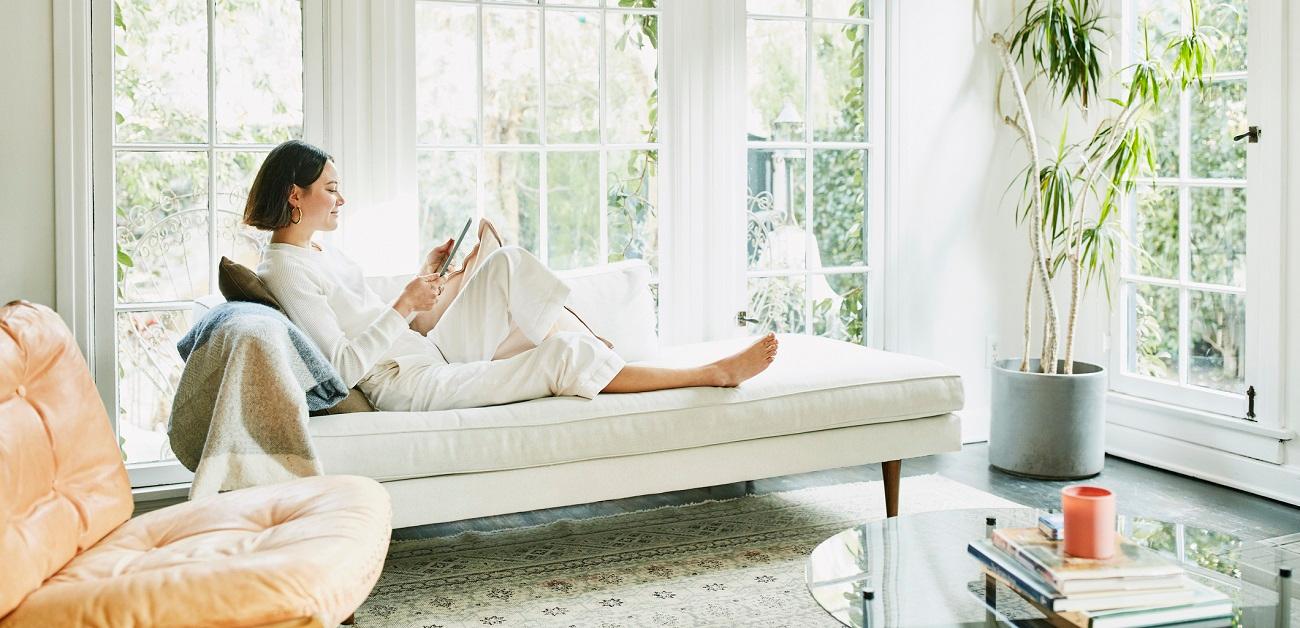 Woman sitting on couch in living room reading on digital tablet