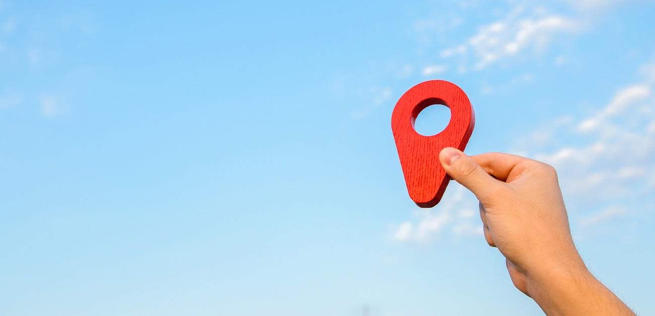 Red location pin in hand on sky background