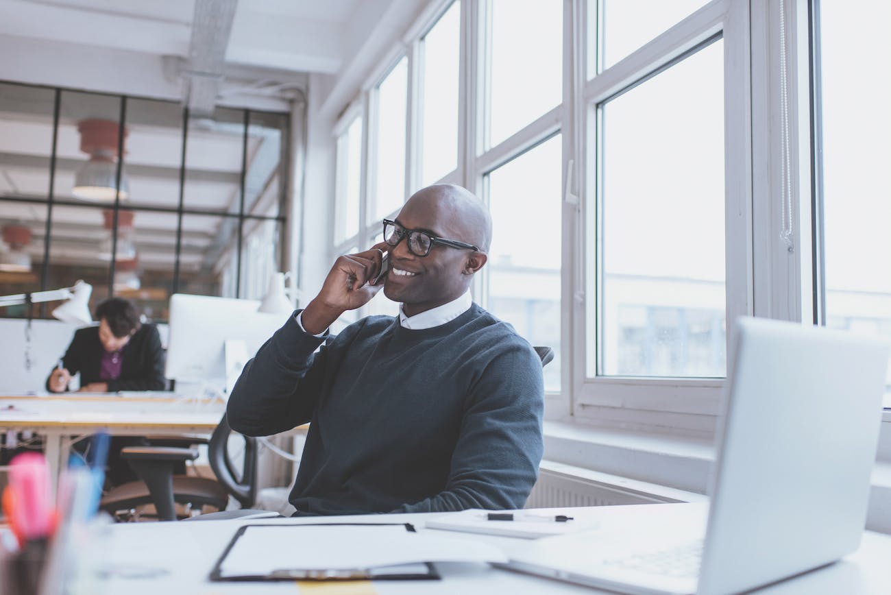 Real Estate Agent Conducting Business in an Office Setting, Talking on the Phone, Working on a Laptop