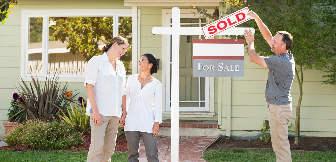 Real estate agent hanging a sold sign in front of house