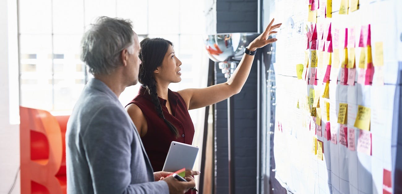 Man and woman looking at colorful adhesive notes on whiteboard