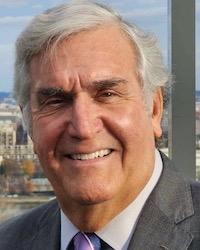 Photo portrait of a silver-haired man in a dark gray suit with a purple tie