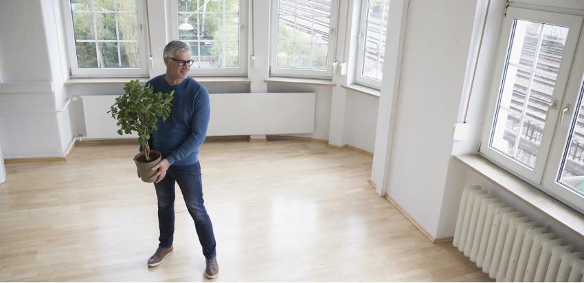 Man standing in an empty apartment holding a plant