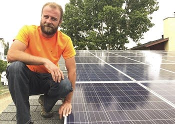 A man on a roof next to roof solar panels