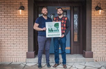 Two men holding a Youngstown Neighborhood Development Corporation sign in front of a renovated home