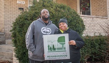 A couple holding a Youngstown Neighborhood Development Corporation sign in front of a renovated home