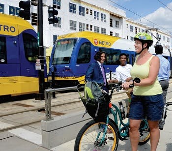 Woman off her bicycle on a sidewalk next to light rail car