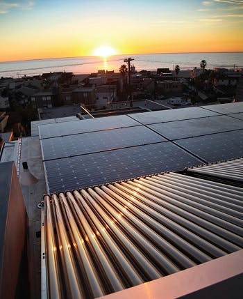 Solar panels on a roof with the sun setting in the background