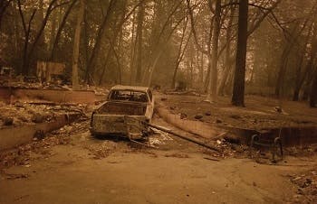 Camp fire aftermath in Paradise, CA showing a burned car and burning trees