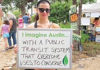 A woman holding up a sign that says "Imagine Austin with a public transportation system that everyone uses, to conserve"