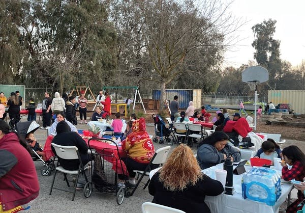 A community meeting gathering families seating at tables in an outdoor area