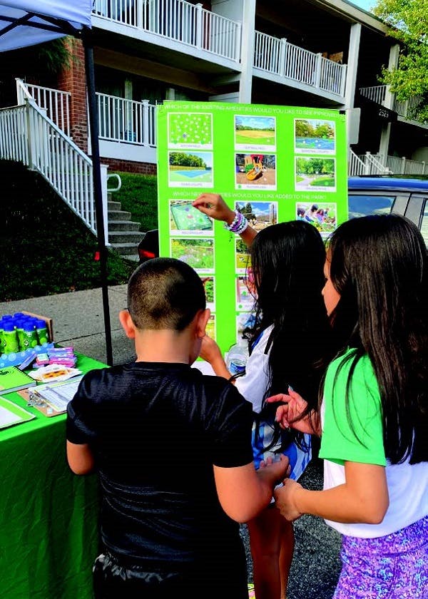 Kids in a park writing and gathering around an announcement board filled with pictures